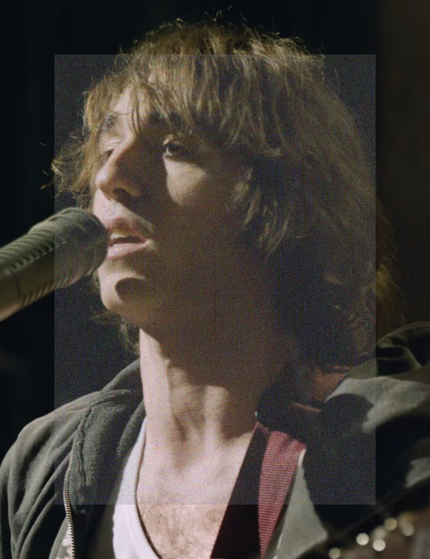 A close up portrait image, low angle shot of Cameron Winter singing into a microphone, with the head of his guitar in the bottom right corner. A rectangle of fine grainy static lightly veils the center of the image.