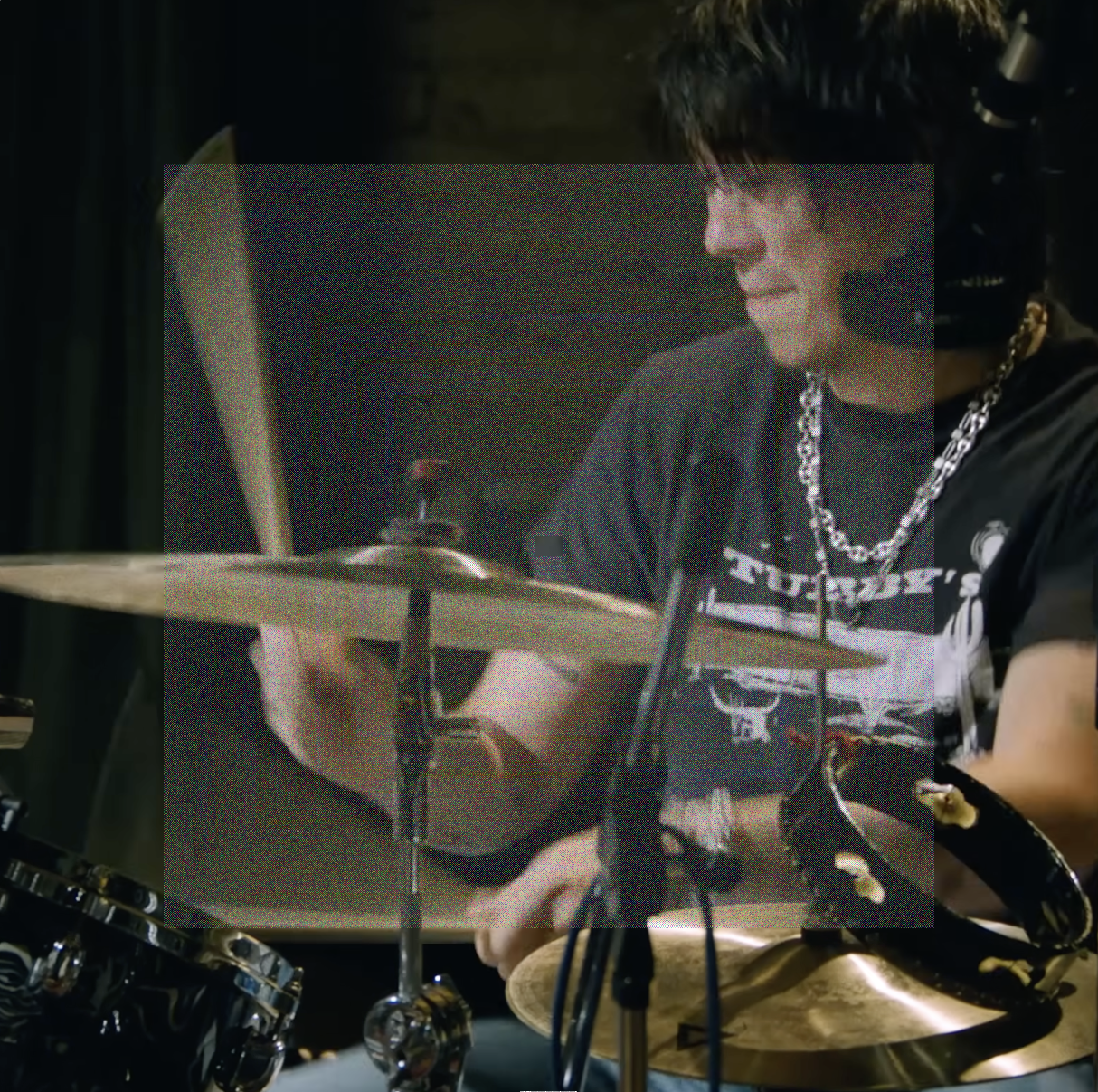 A close up square image of Max Bassin intensely playing the drums. A square of fine grainy static lightly veils the center of the image.