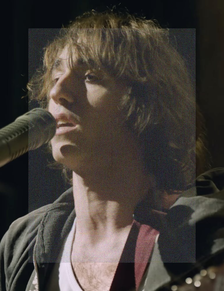 A close up portrait image, low angle shot of Cameron Winter singing into a microphone, with the head of his guitar in the bottom right corner. A rectangle of fine grainy static lightly veils the center of the image.