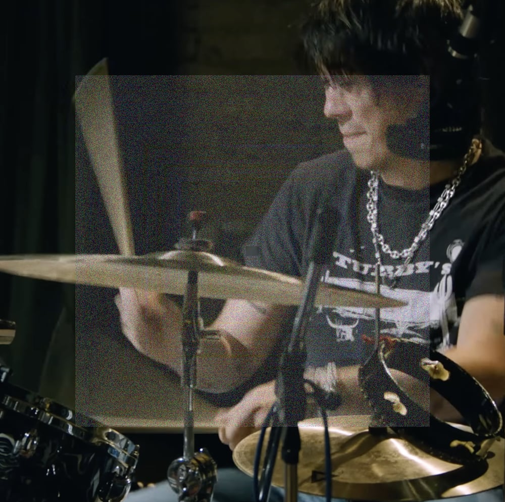 A close up square image of Max Bassin intensely playing the drums. A square of fine grainy static lightly veils the center of the image.