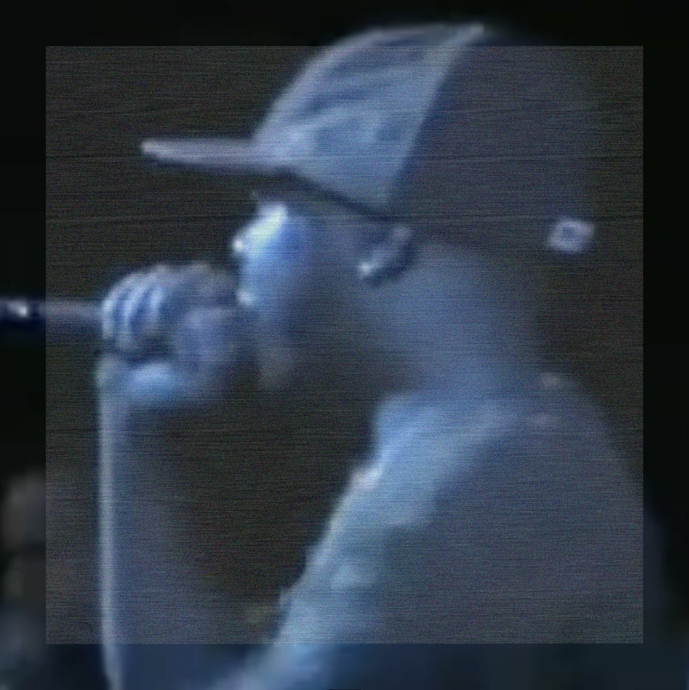A lofi close-up of J Dilla holding a microphone to his mouth, looking left, wearing a ballcap in a live stage setting. The image is cast in a cool blue-gray wash; a large centered square of fine horizontal scanline noise covers most of the frame, only faintly distinguishable from the darker, smoother border surrounding it.