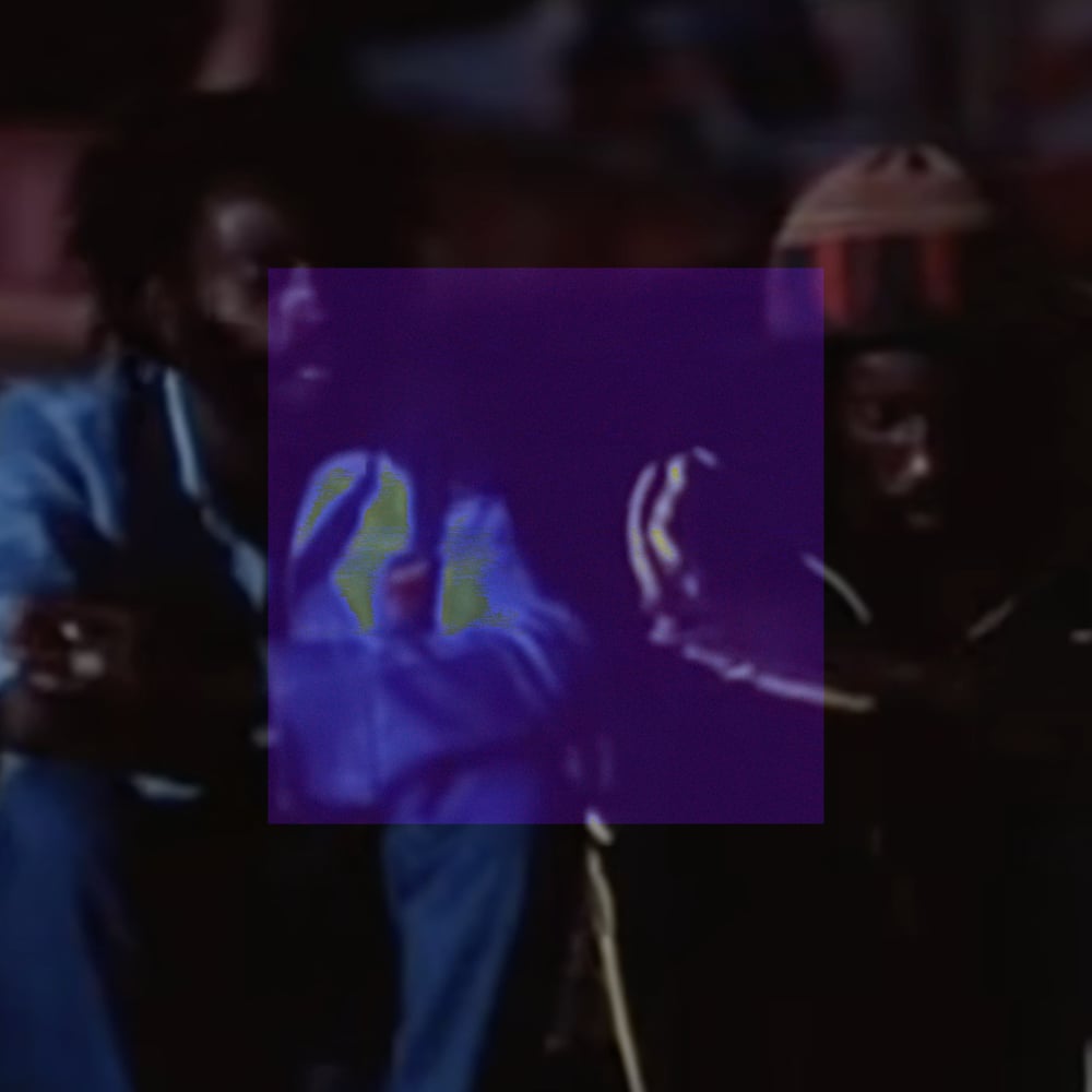 A dim, low-contrast performance photograph showing several figures in a dark indoor setting. A centered deep violet-purple square covers the middle third of the image, rendering the figures within it as blue-purple shapes with faint lime-yellow highlights. To the left, a figure in light blue clothing is visible outside the distortion. The surrounding image is dark and muted with warm reddish ambient light.